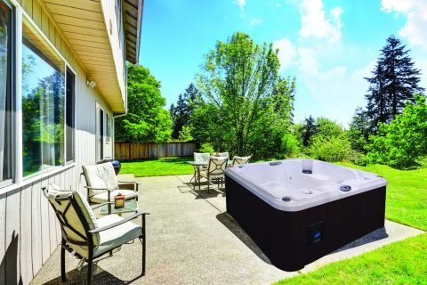 Backyard concrete floor patio area with hot tub. Well kept lawn around. Northwest, USA